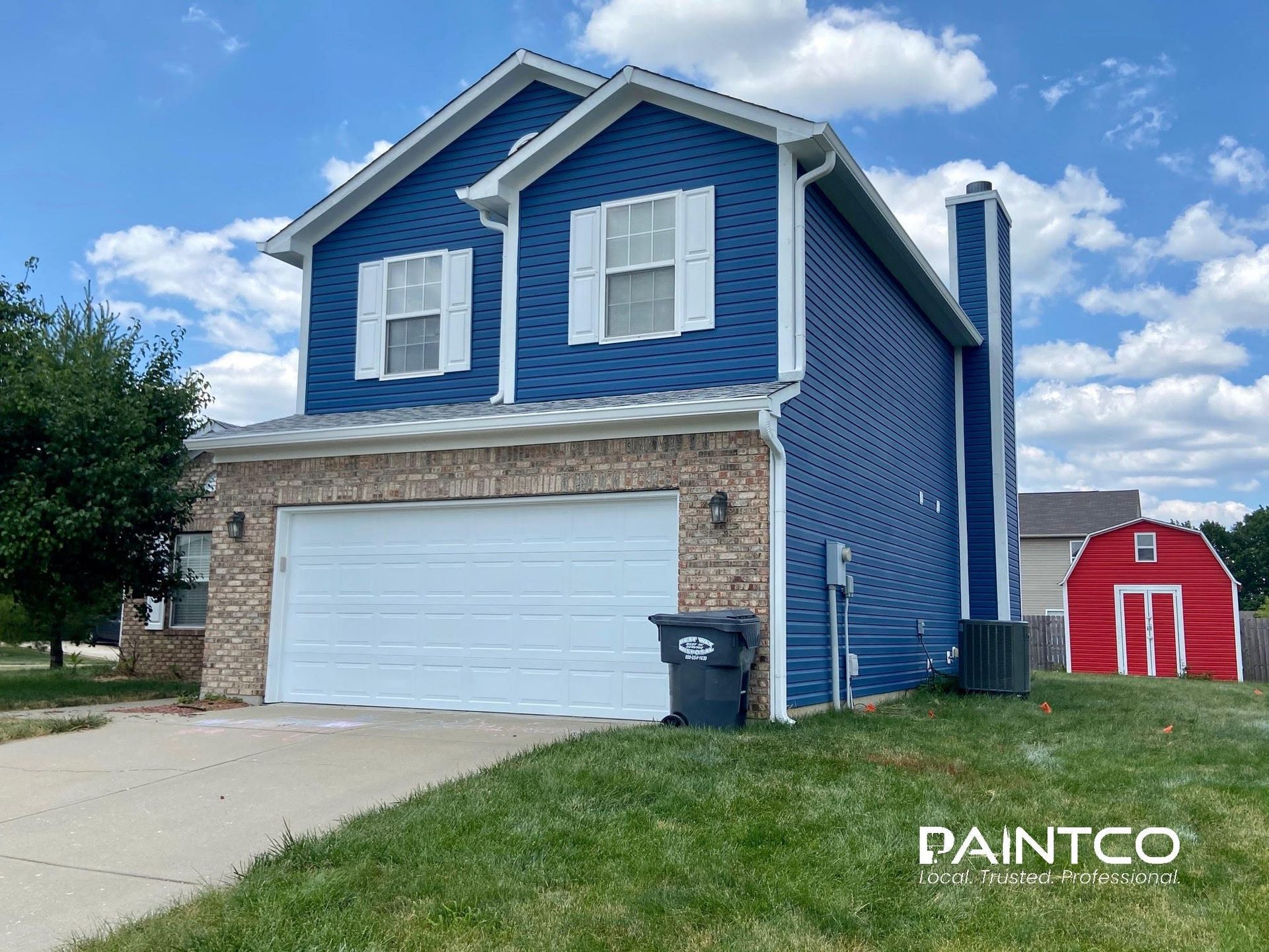 Two-story blue house with white trim, a garage, and a red barn in the background.