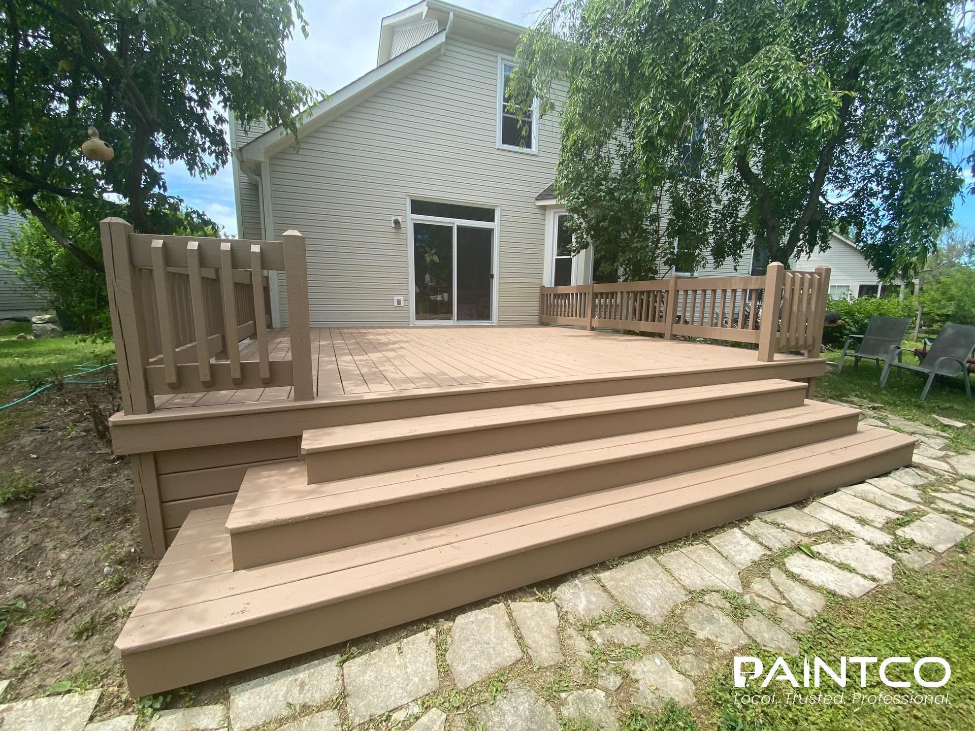 A wooden deck with steps leading to a house with a sliding door. The deck is brown.
