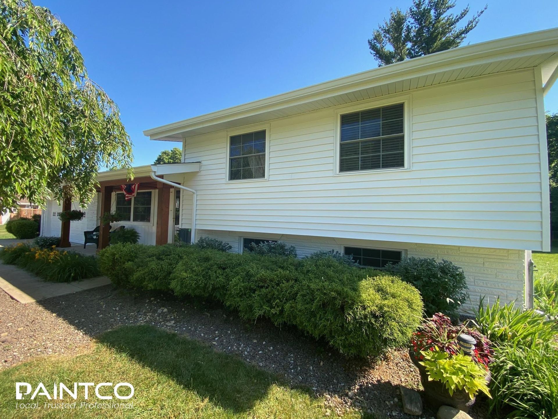 White house with manicured bushes and landscaping under a bright blue sky.
