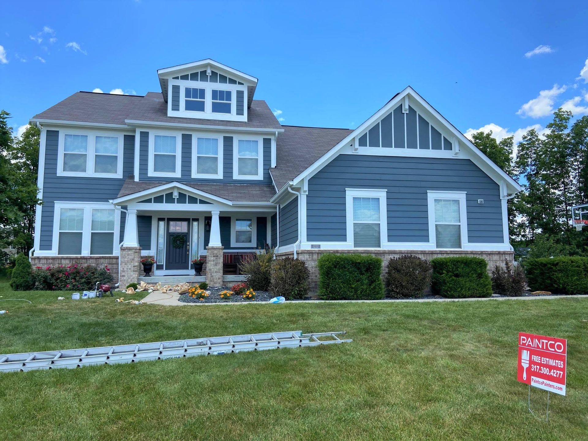 Blue house with white trim, brick accents, and landscaping on a sunny day. A 