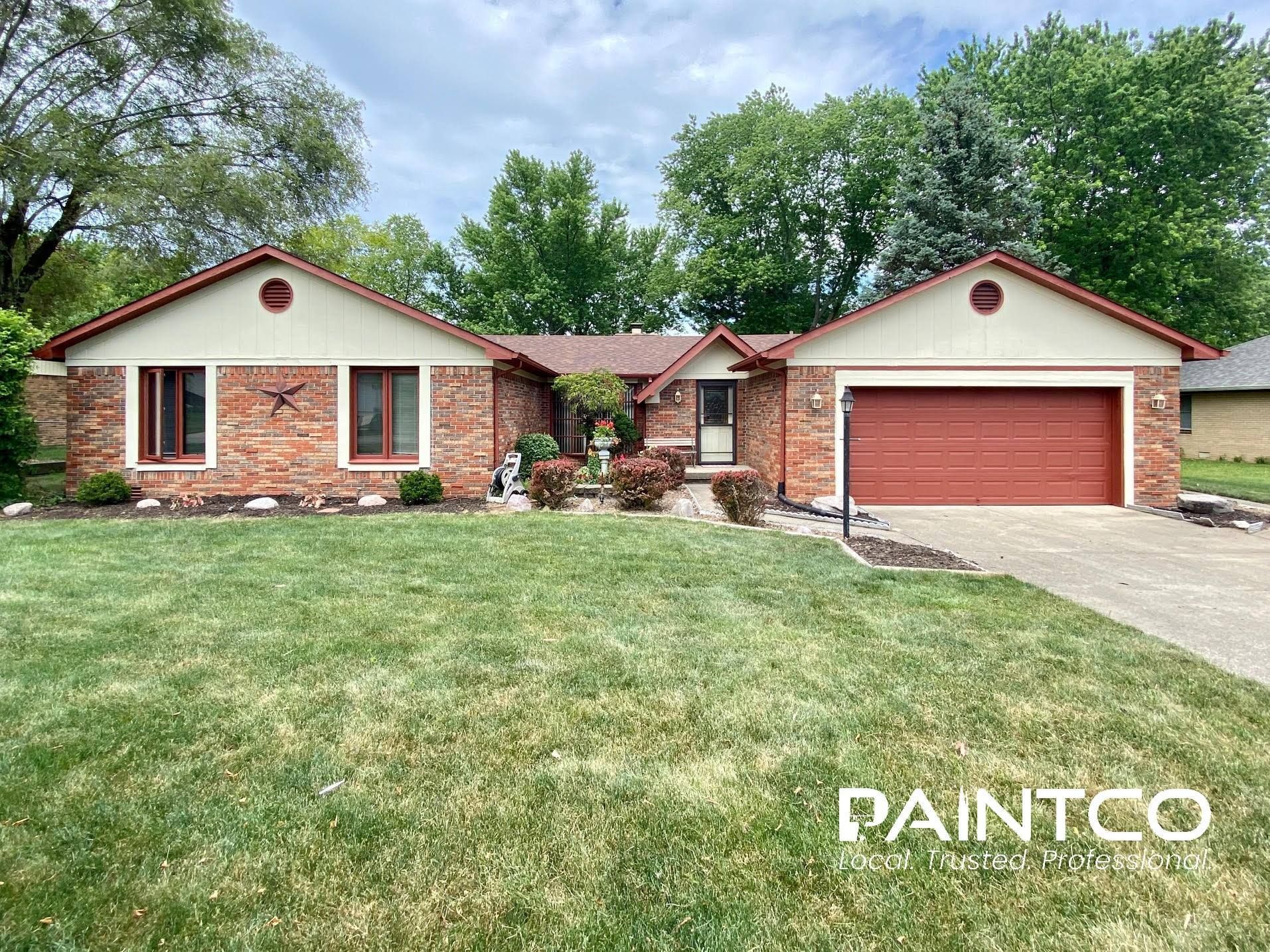Ranch-style house with red brick and trim, beige siding, and red roof, with green lawn and trees.