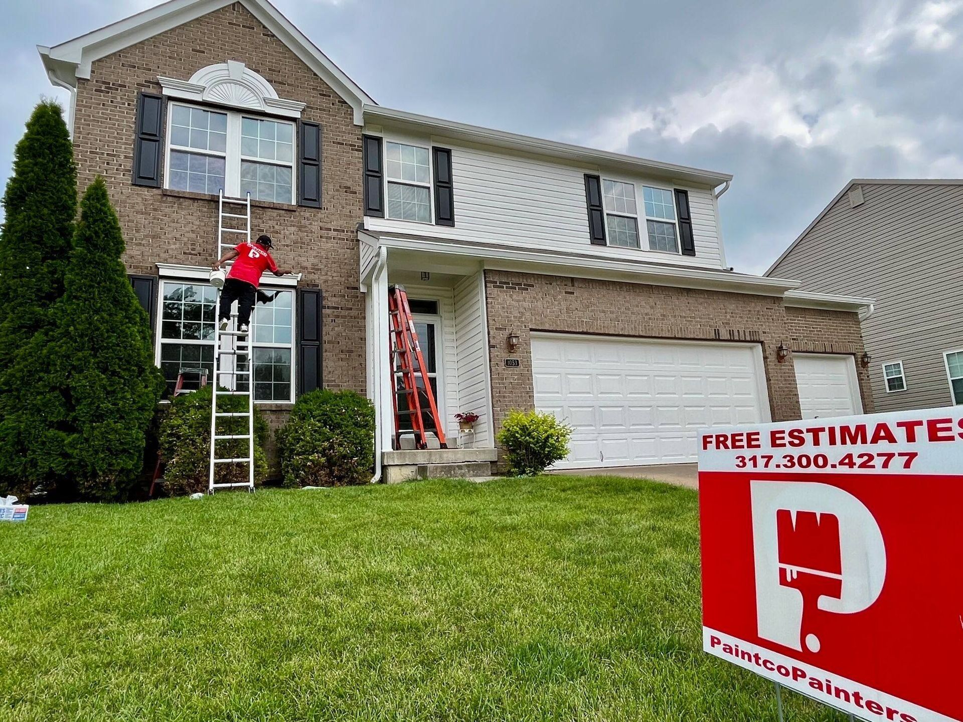 House being painted by a worker on a ladder; red sign in front with painter logo and phone number.