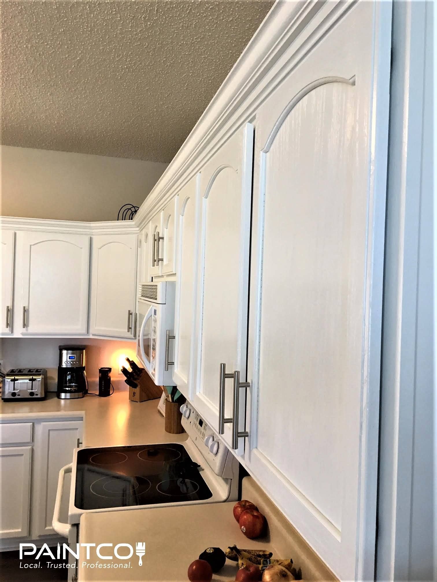 White kitchen cabinets with arched panels, above a countertop and appliances.