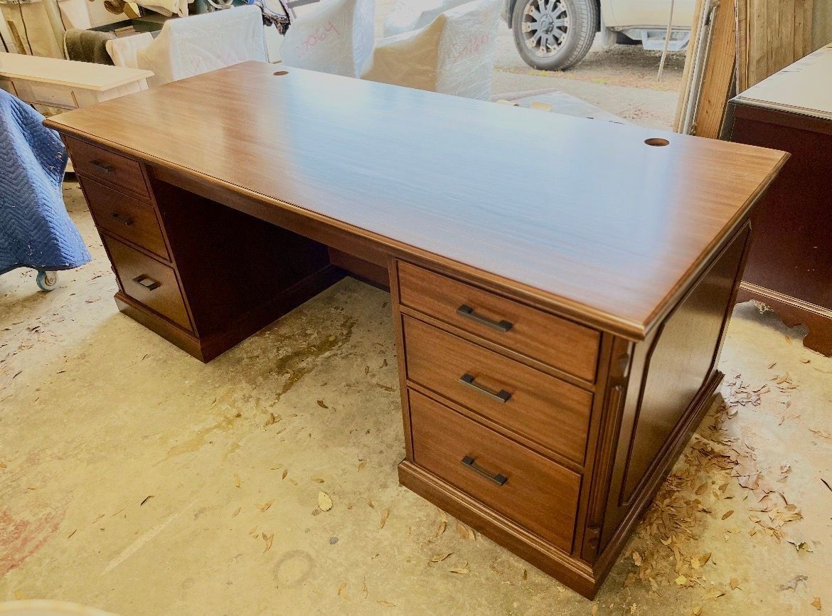 A large, wooden executive desk with a rectangular top and two pedestals, each featuring three drawers, in a workshop.