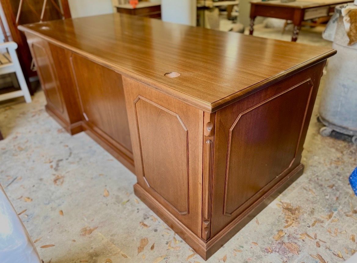 A large, brown wooden executive desk with detailed molding on the side panels, positioned in a workspace.