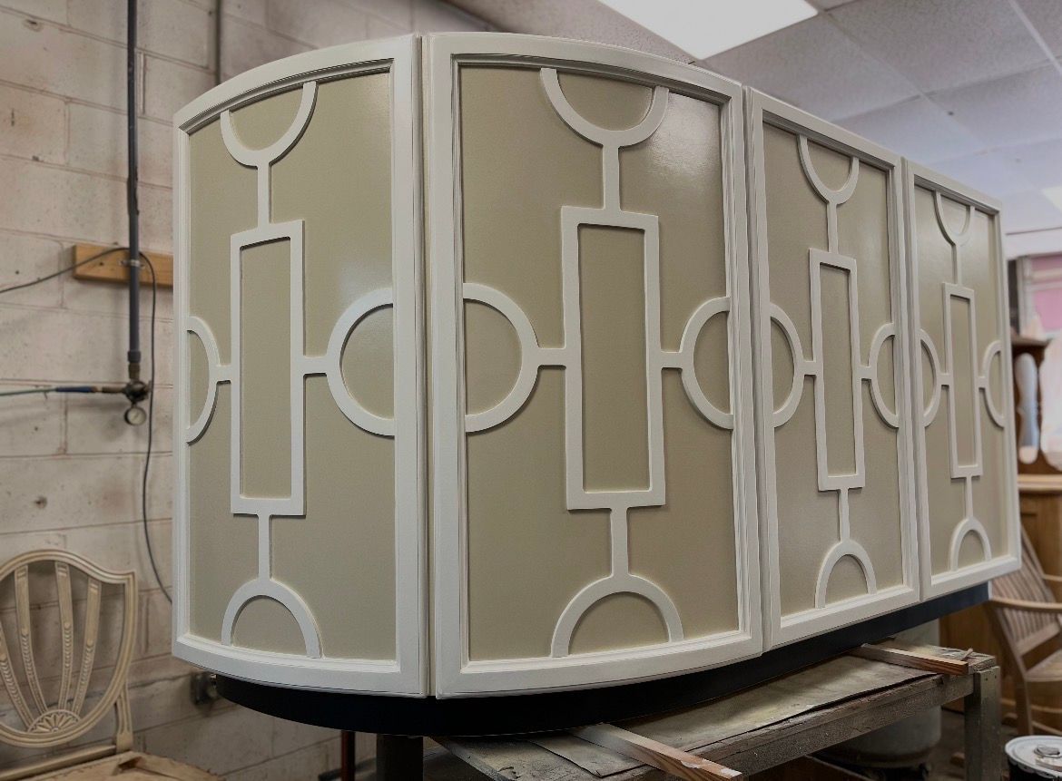 A curved, cream-colored cabinet with white geometric latticework trim in a workshop setting.
