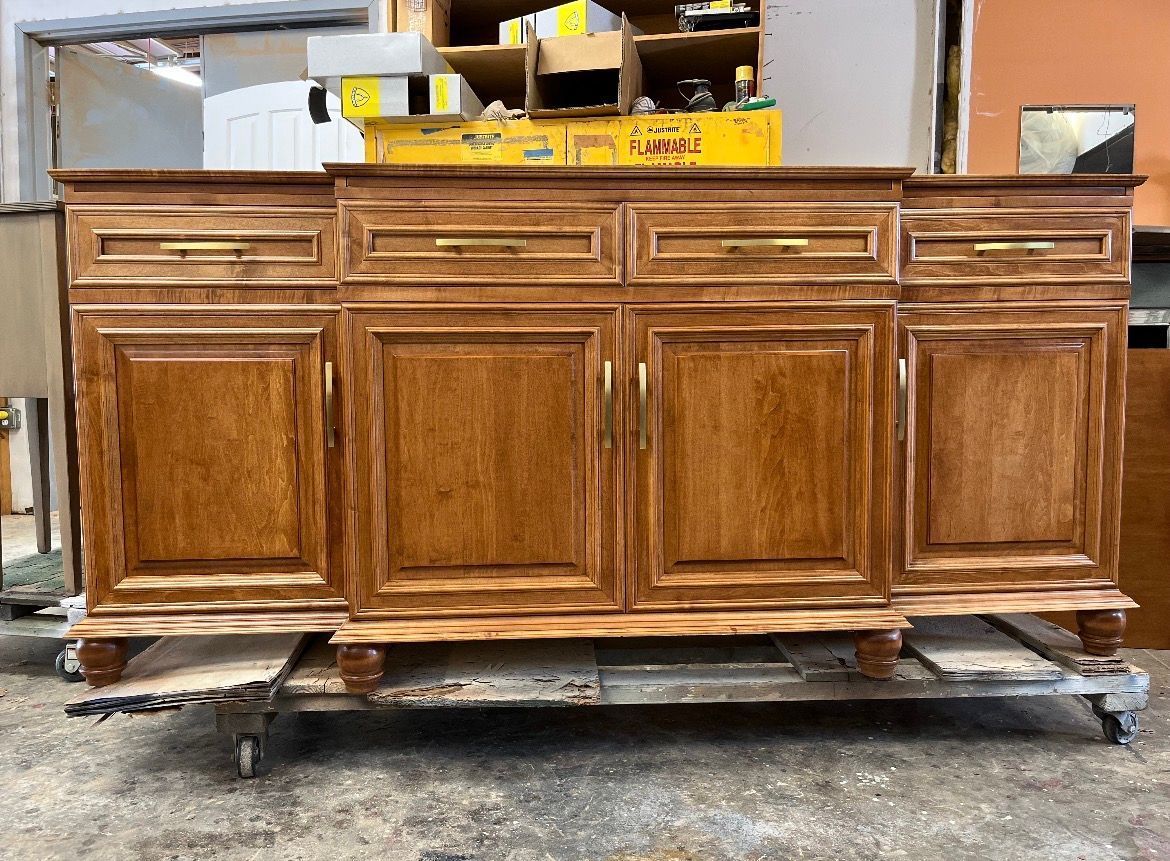 A four-door wooden sideboard with brass handles and drawers, resting on a rolling cart in a workshop setting.