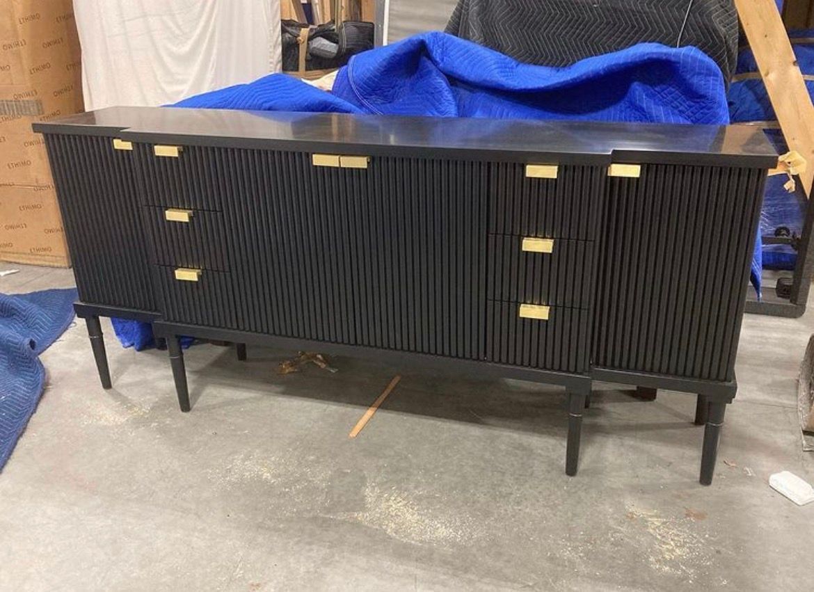 A black, multi-door sideboard with vertical textured detailing and gold rectangular hardware, standing on four legs.