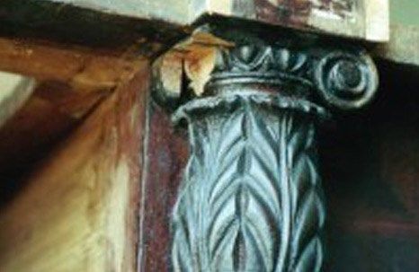 Dark wooden decorative column with carved leaves and a cracked top.