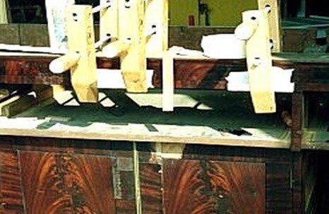 Wooden clamps securing wooden pieces to a cabinet's surface during furniture repair.