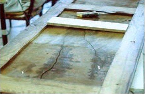 Cracked wooden door with a white board and screwdriver on top, indoors.
