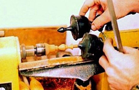 A person using a wood lathe to shape a small, wooden object. Hands are holding the object and a tool.