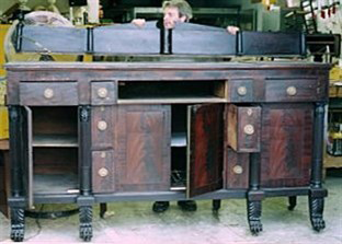 A person in a woodworking shop, with an antique wooden sideboard opened.