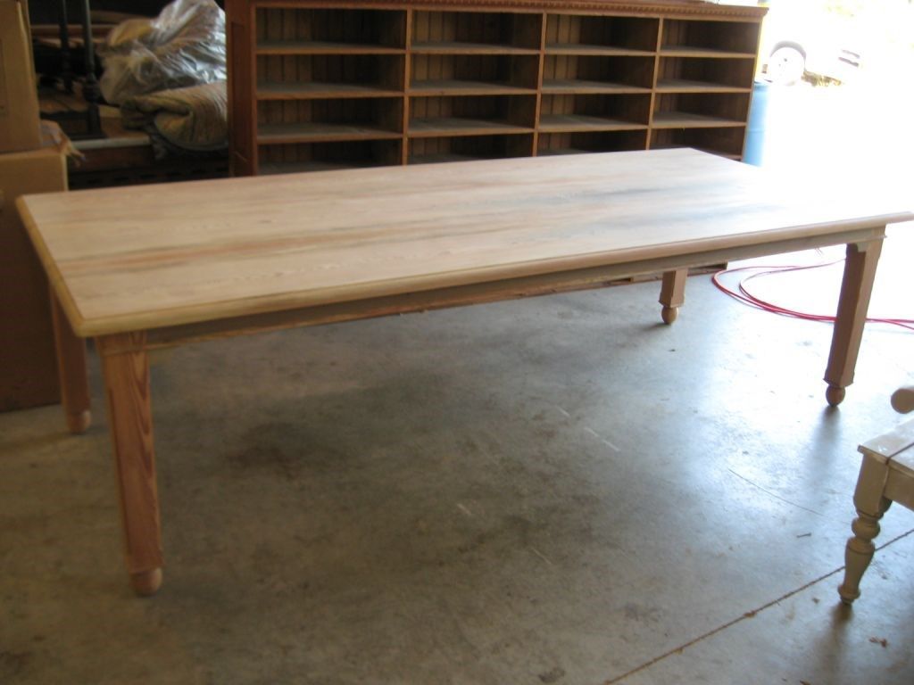 Wooden dining table, unfinished, with turned legs, in a workshop setting.