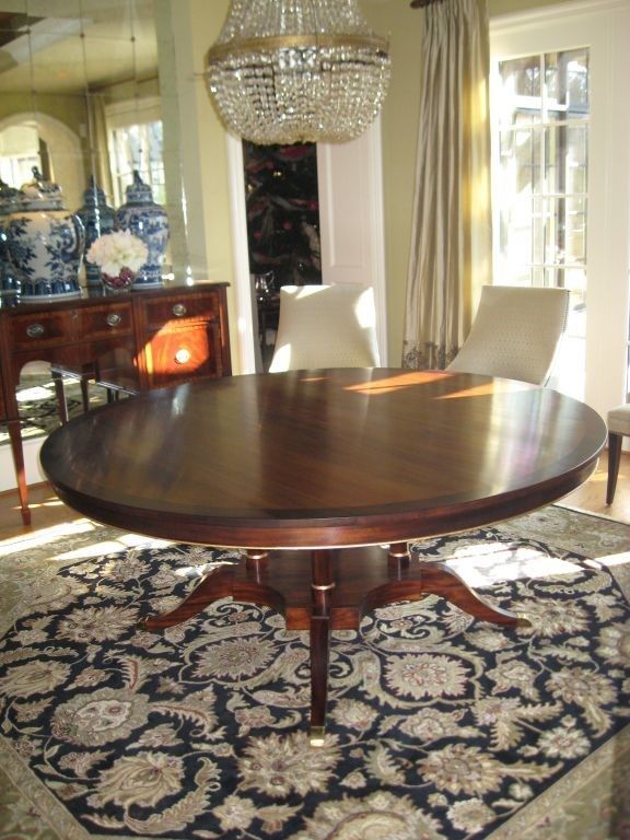 Round, dark wood dining table on a floral rug, beneath a crystal chandelier.