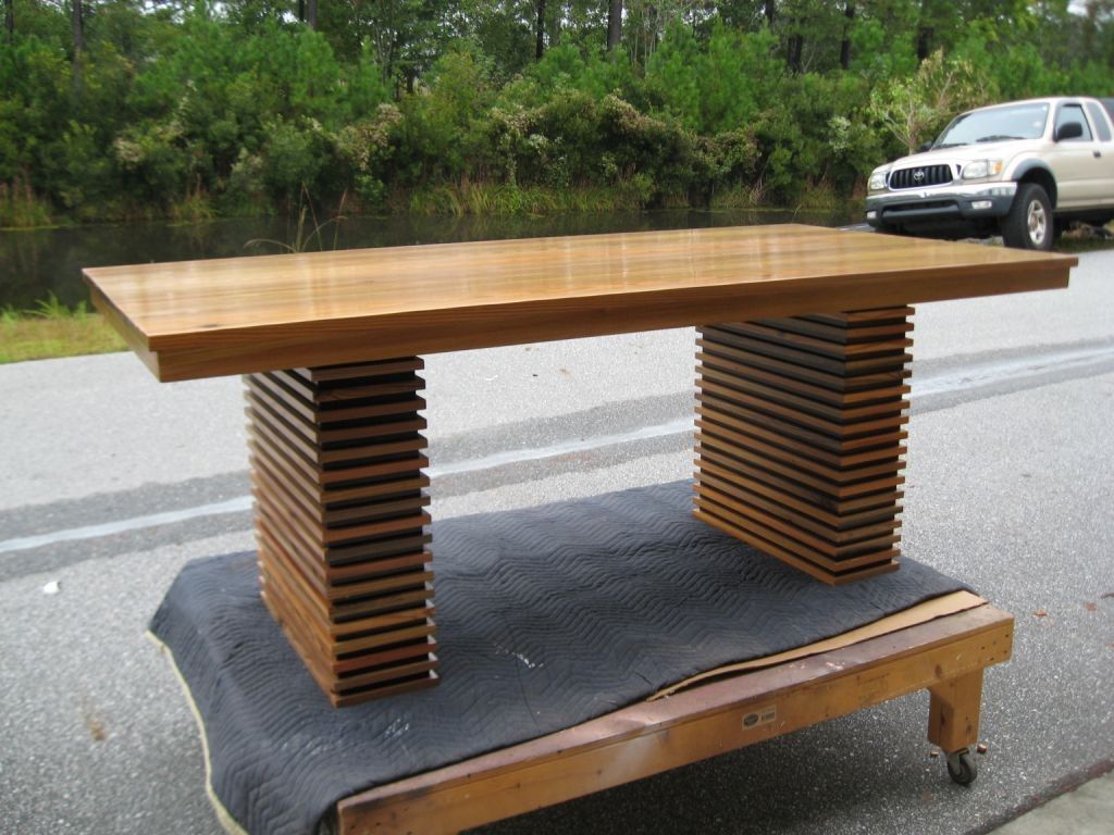Wooden desk with layered rectangular legs and a long, flat tabletop, outdoors.