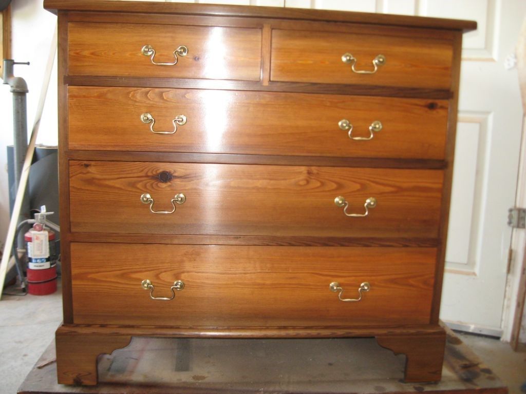 Chest of drawers with five drawers and brass handles, made of wood with a warm, glossy finish.