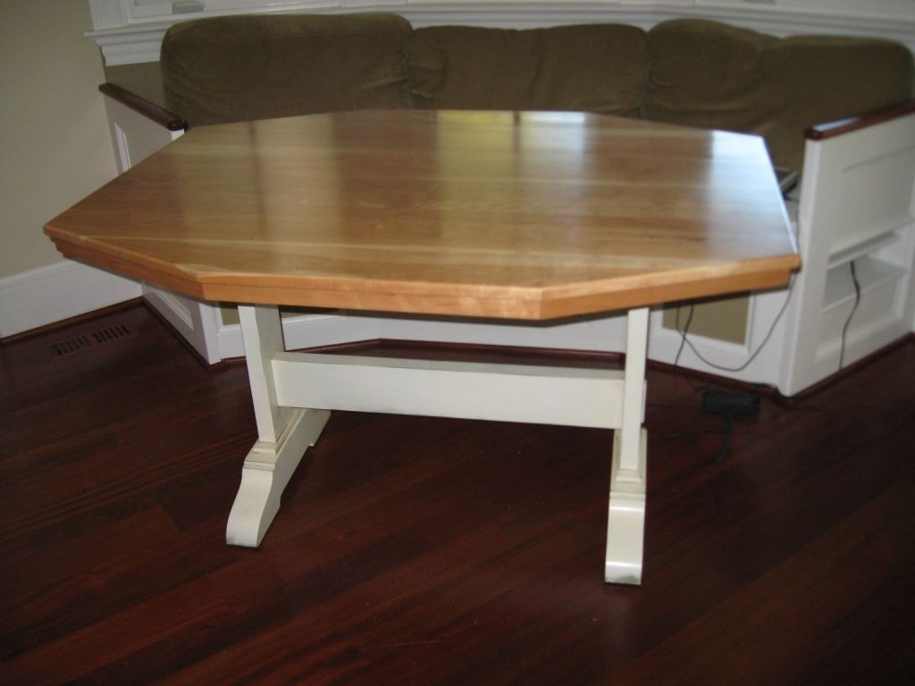 Octagonal wooden table with light wood top and white base in a room.