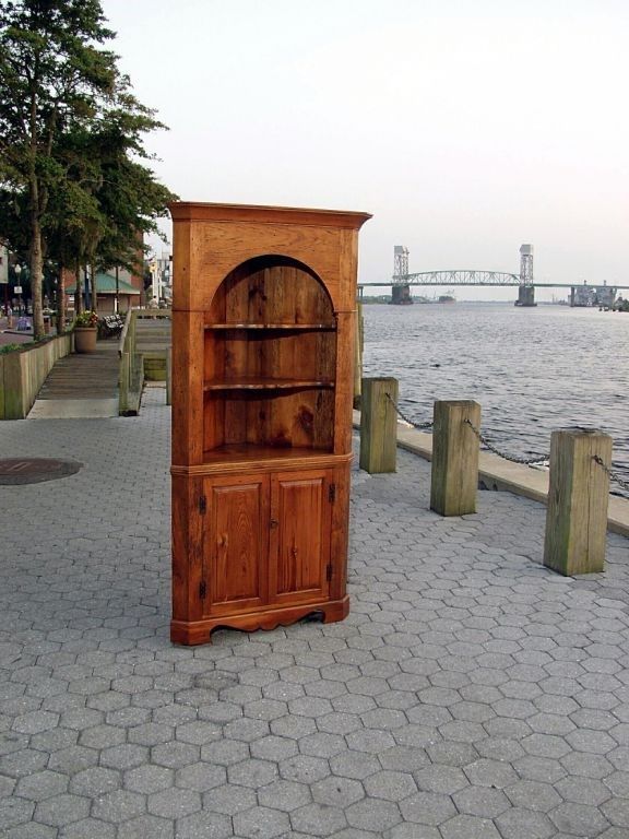 Wooden corner cabinet on a brick waterfront, with bridge in the background.