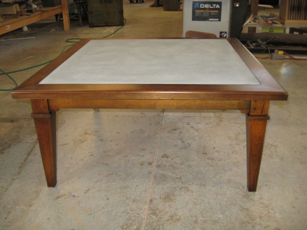 Square wooden table with a light gray center and brown frame and legs in a workshop.