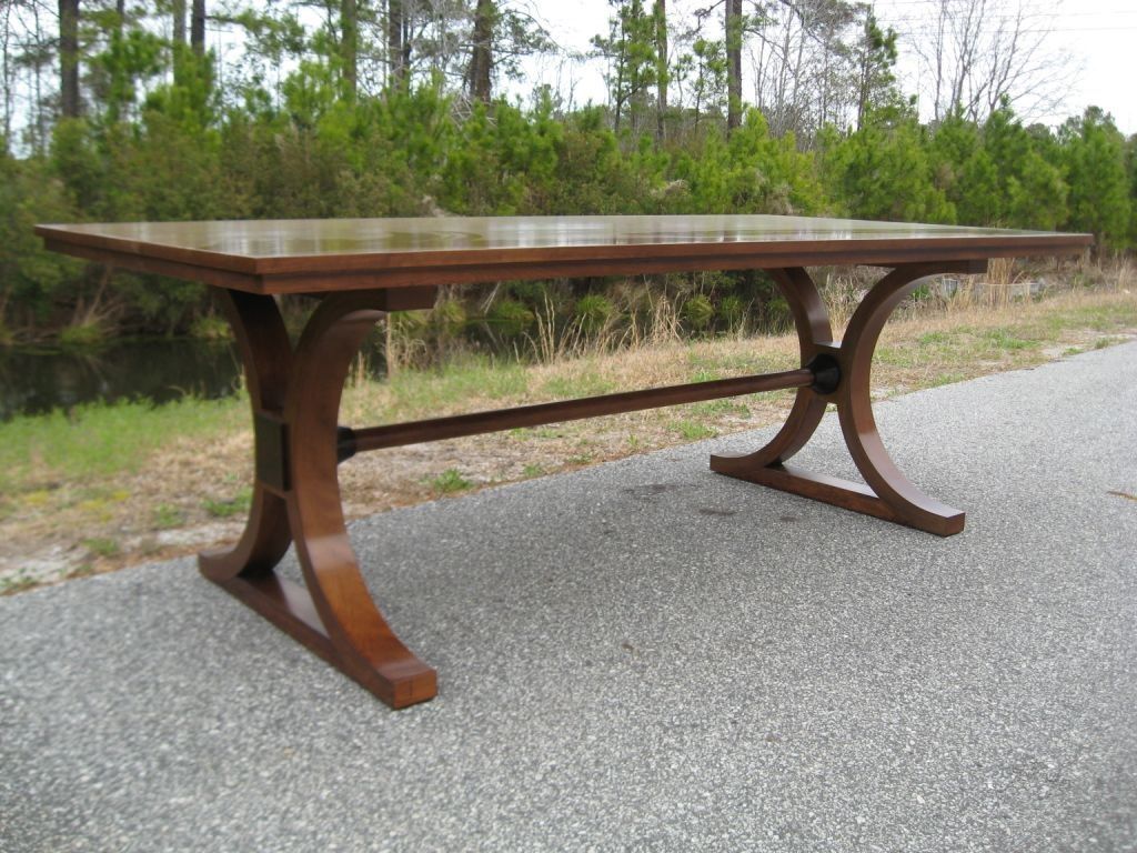 Brown wooden rectangular table on a gravel surface, with arched legs and a cross support.