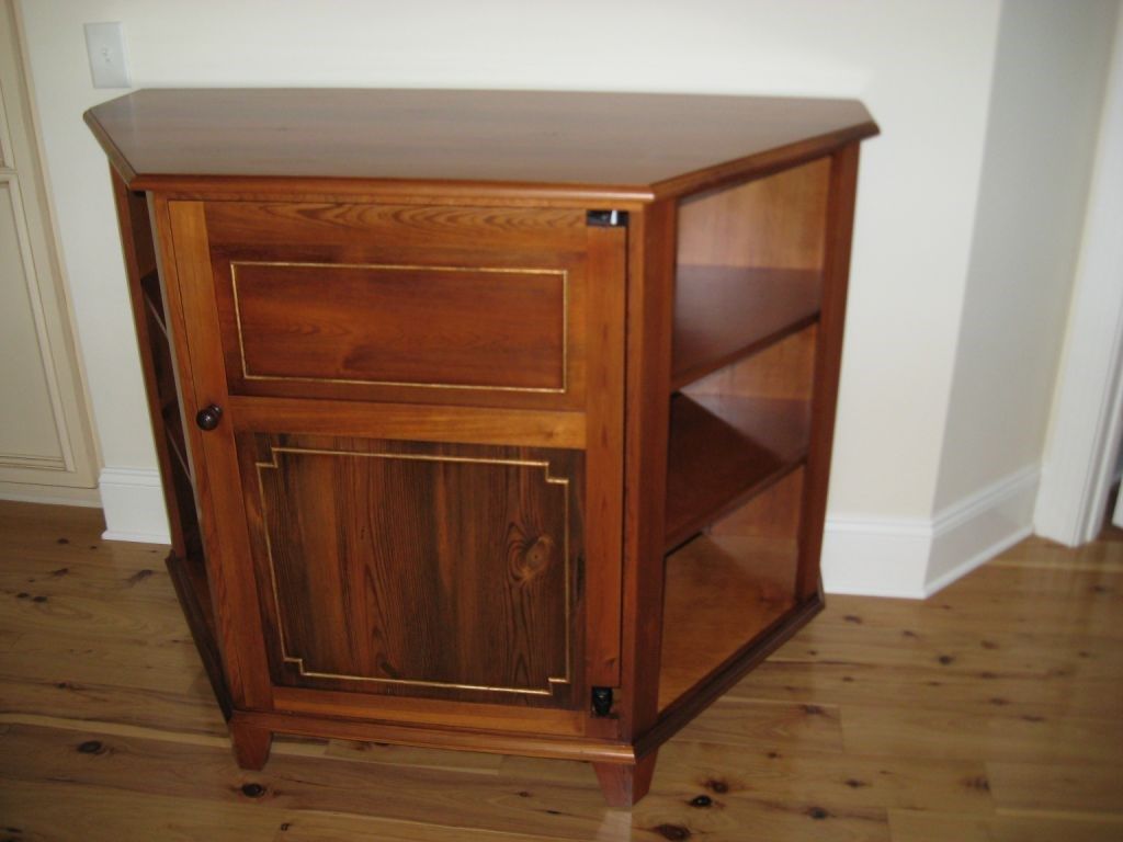 Wooden corner cabinet with shelves and a door, in a room with wood flooring.