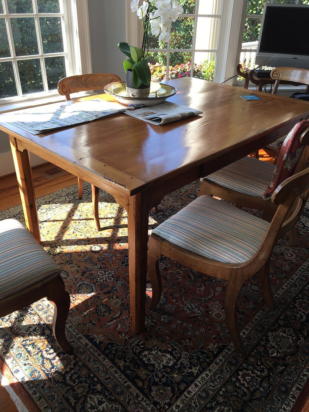 Wooden dining table with four chairs on a patterned rug near a window with sunlight.