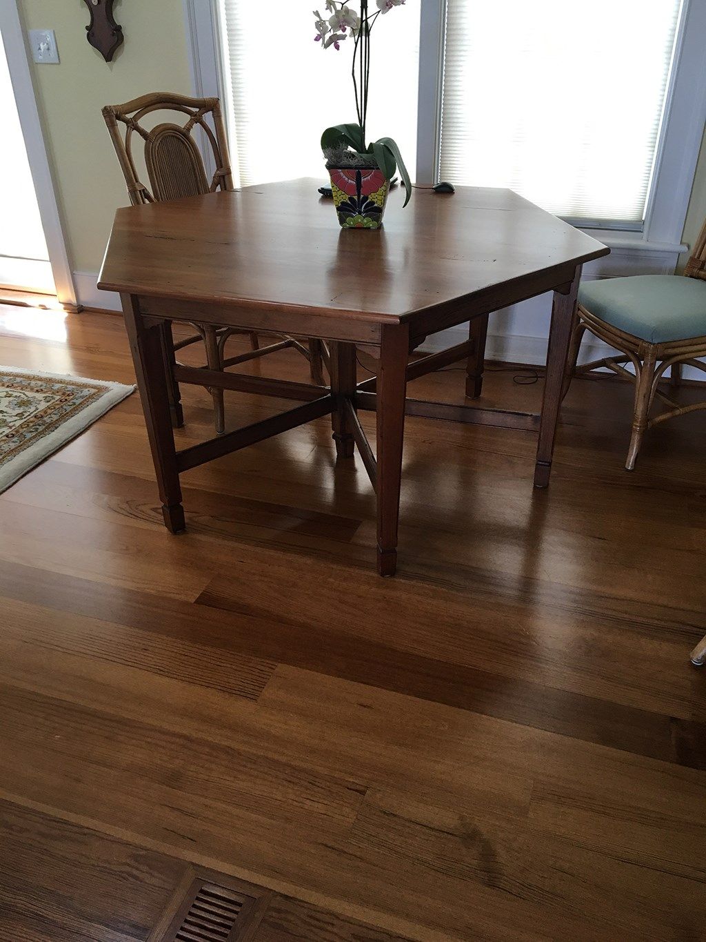 Wooden hexagonal table with two wicker chairs.  Hardwood floor.  Plant with flowers on table.