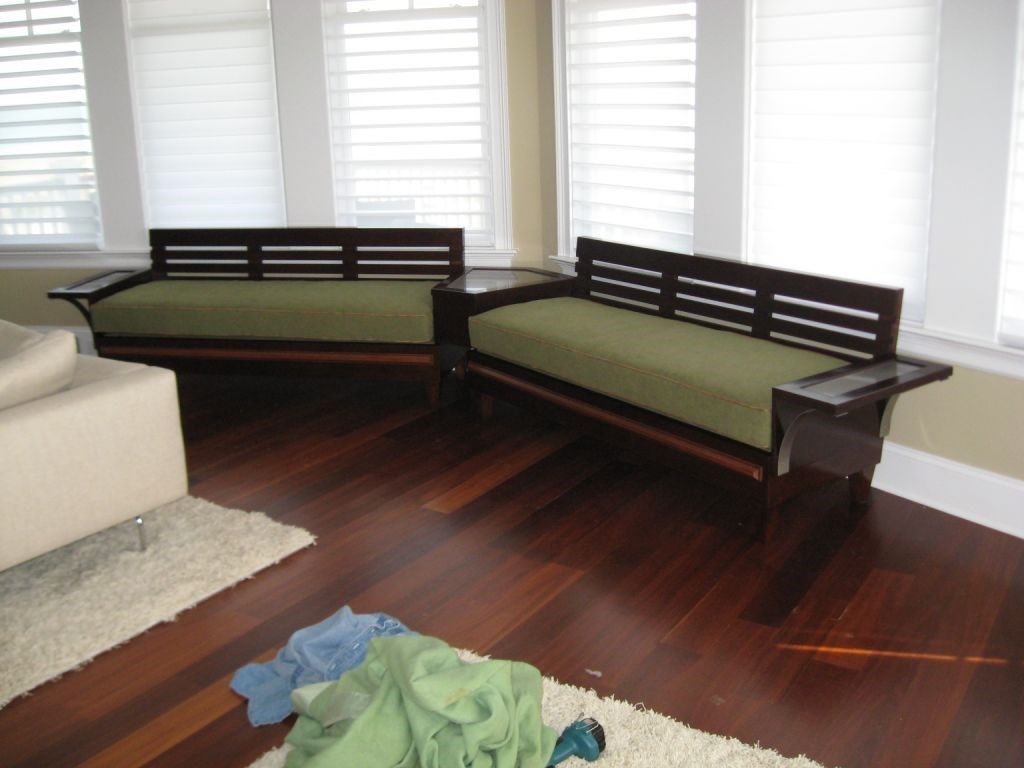 Two wooden sofas with green cushions, dark wood flooring, and white blinds.