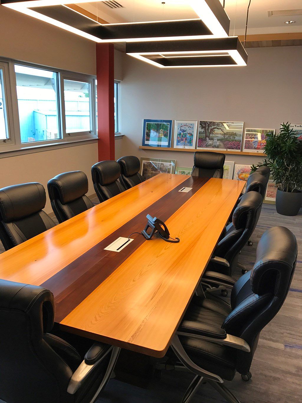 Conference room with long wooden table, black leather chairs, and framed artwork.