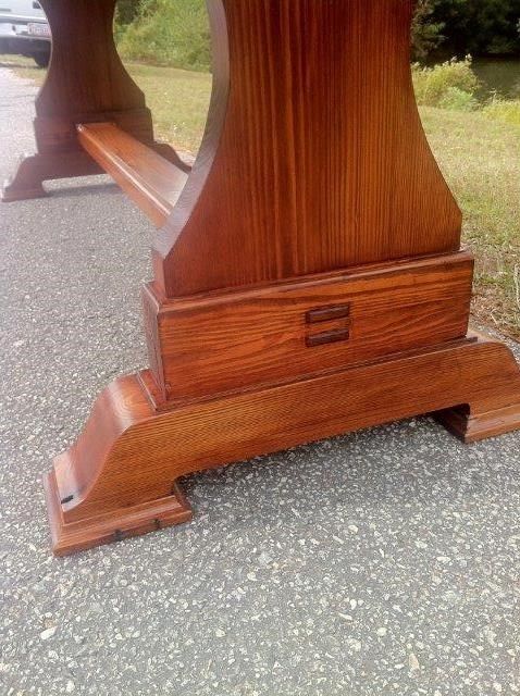 Wooden table leg, medium brown with visible grain, on asphalt.
