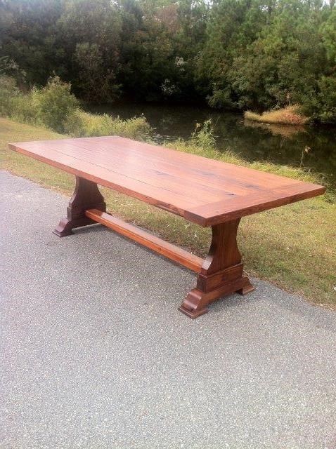 Large wooden trestle table on paved area, with a body of water and trees in the background.