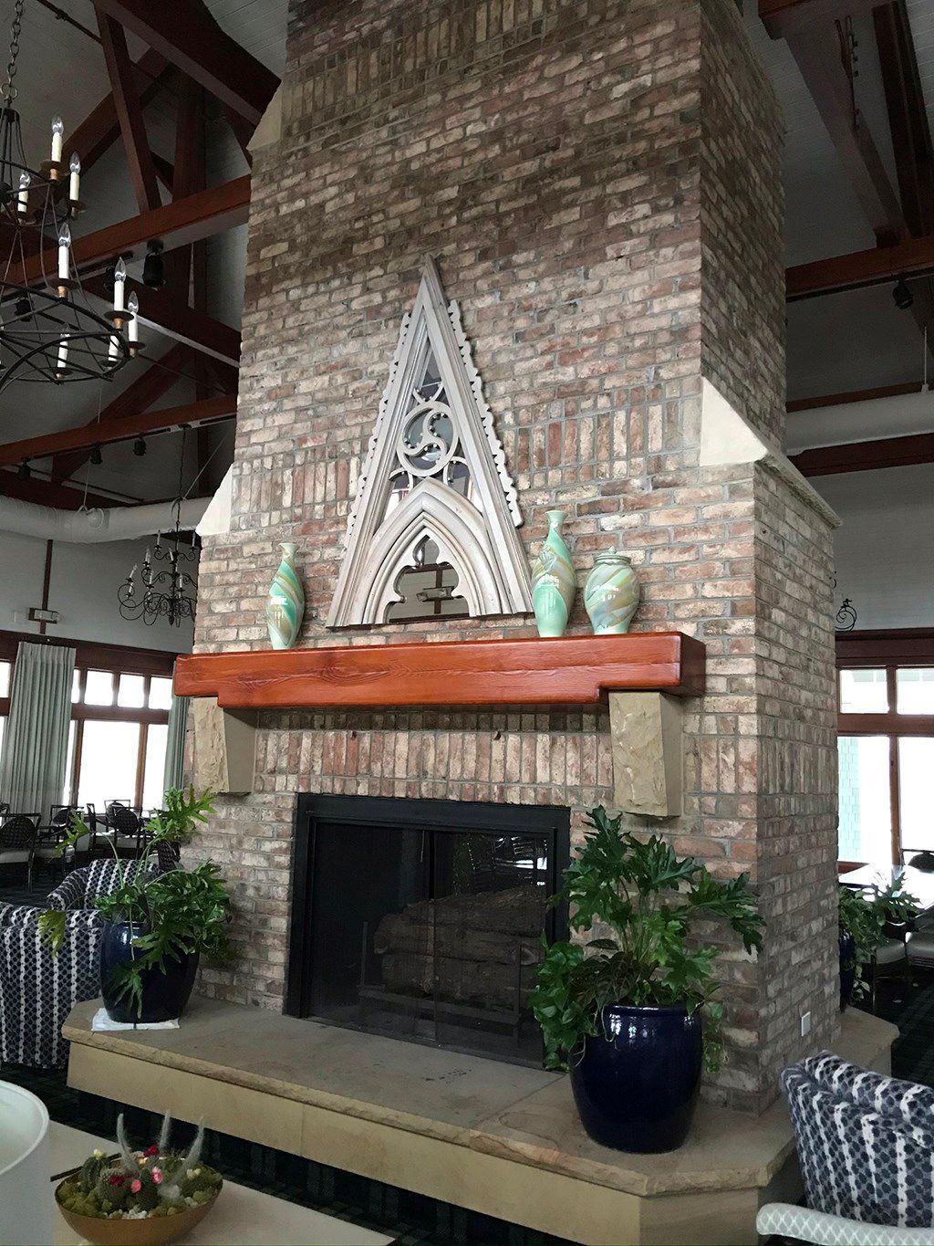 Brick fireplace with wooden mantel, ornate white architectural detail, green vases, and potted plants.