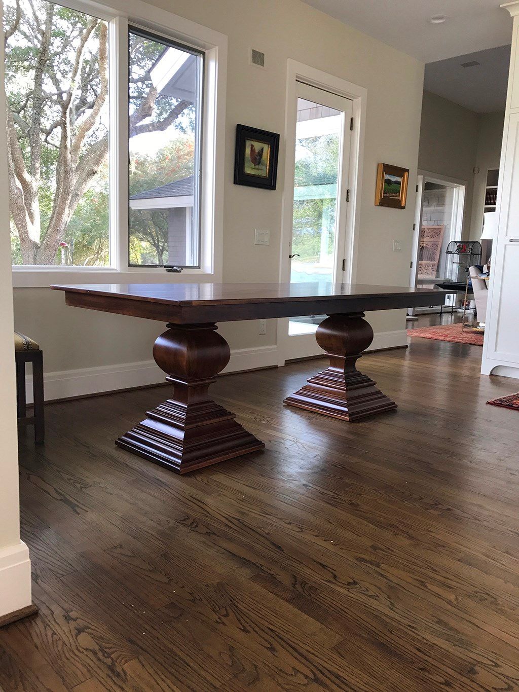 Dark wood dining table with two pedestal bases in a bright room with windows.