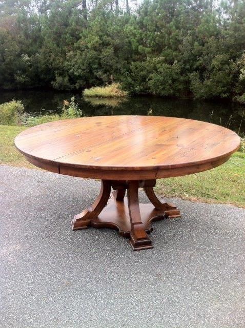 Round wooden dining table on a paved surface, with water and trees in the background.