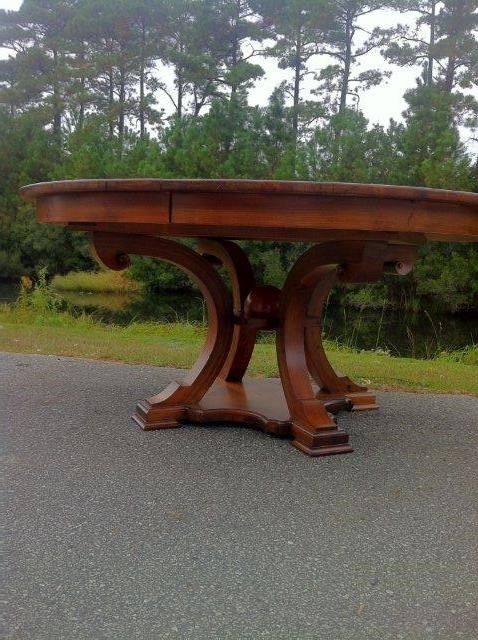 A large, round, dark wood table on an asphalt surface, with a forested background.