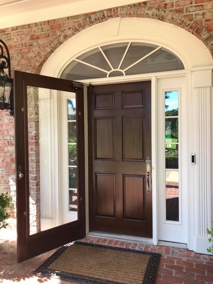 Open brown front door with glass sidelights and arched transom, set in a brick and white trim doorway.