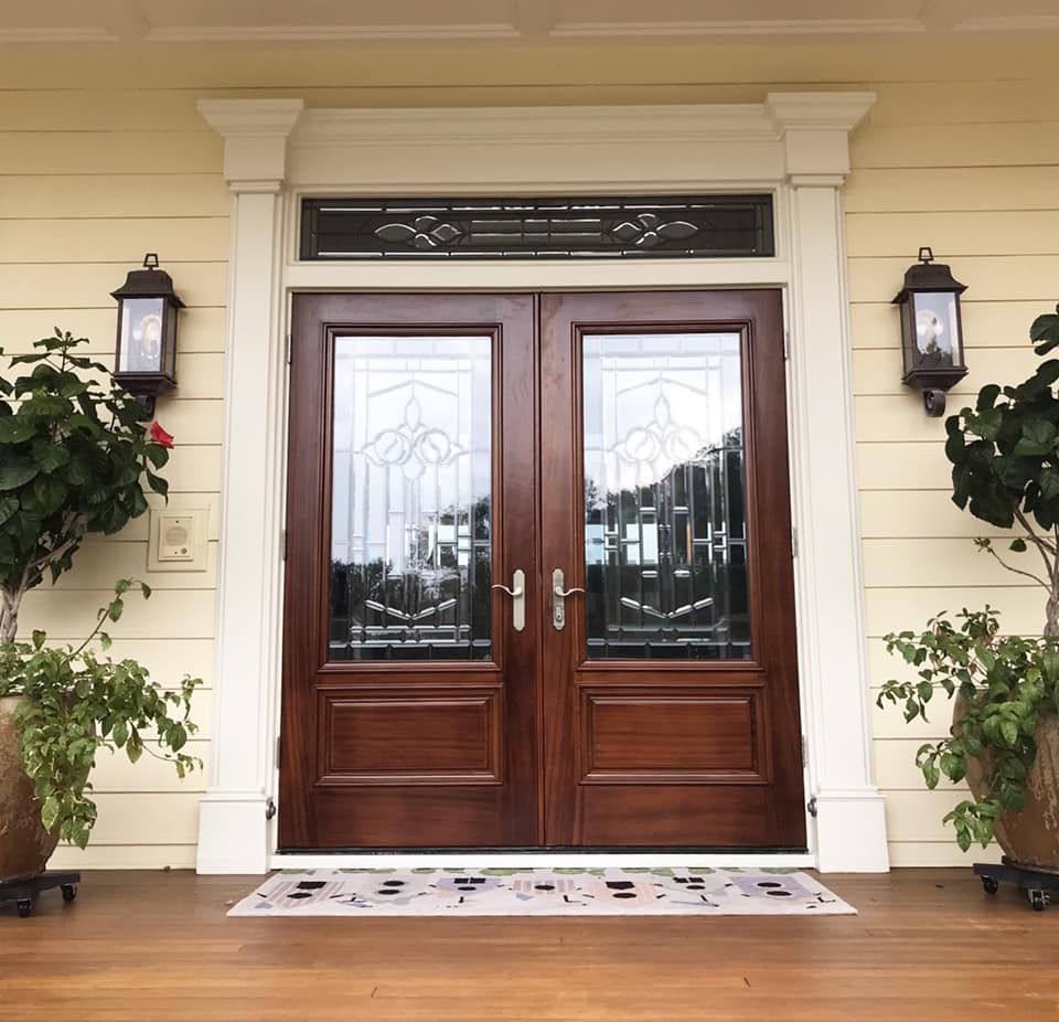 Double wooden front doors with glass panels, flanked by lights and potted plants.