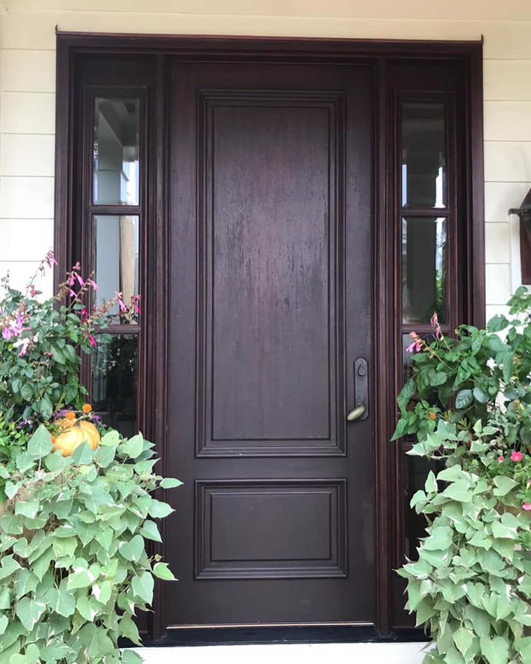 Dark wood front door with sidelights, flanked by green and pink potted plants.