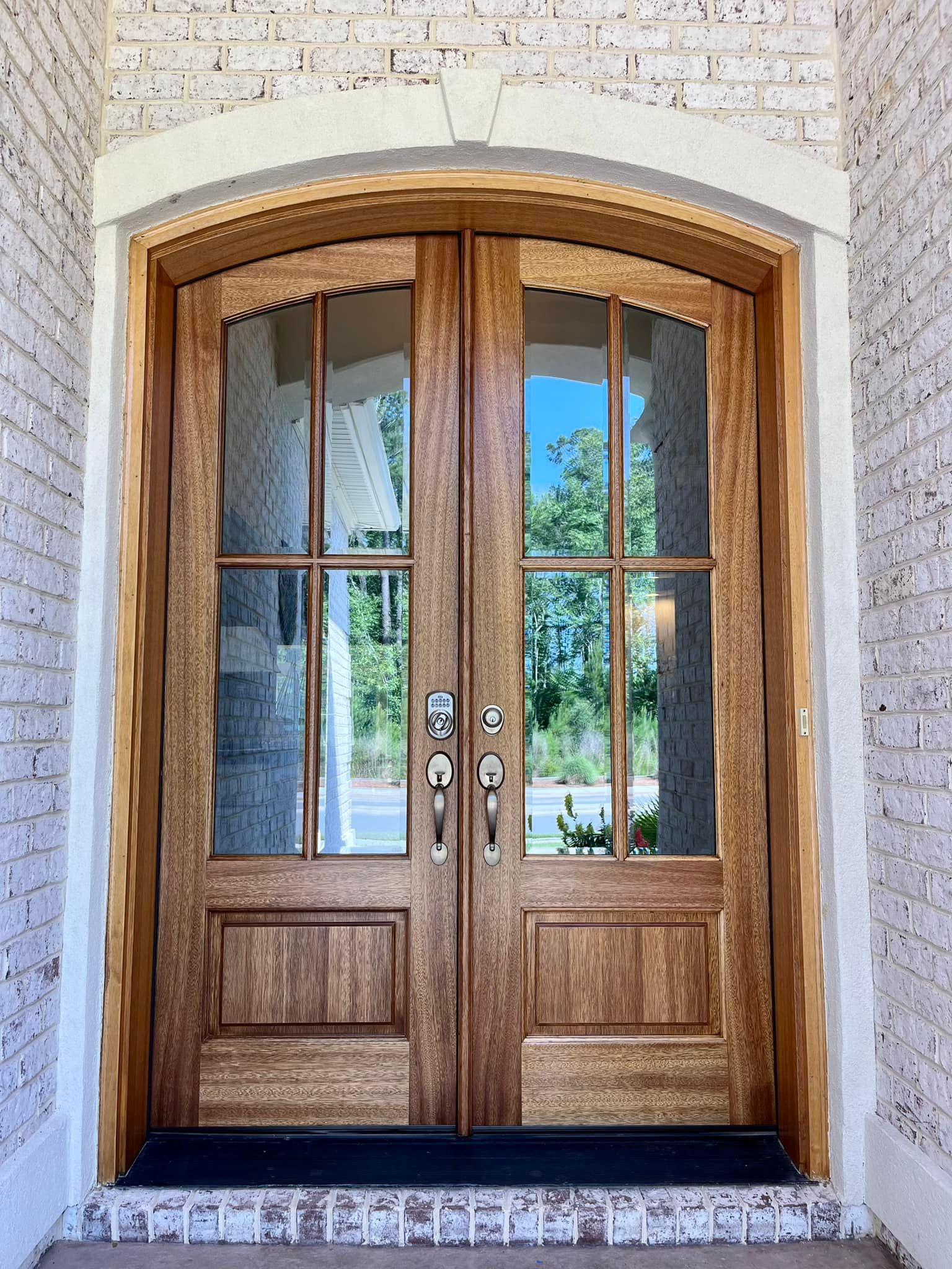 Double wooden front doors with arched glass panels, set in a white brick entryway.