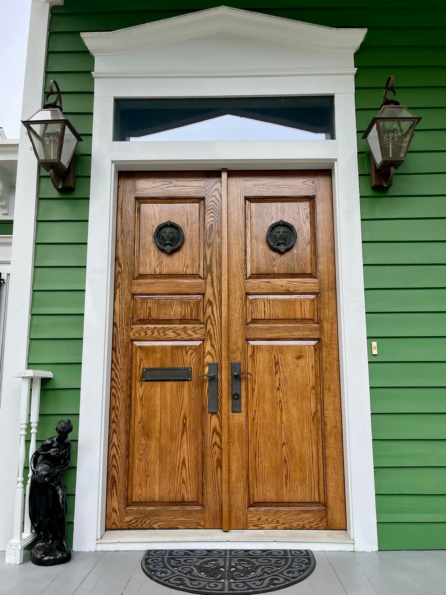Wooden double doors with dark hardware, green siding, and white trim.