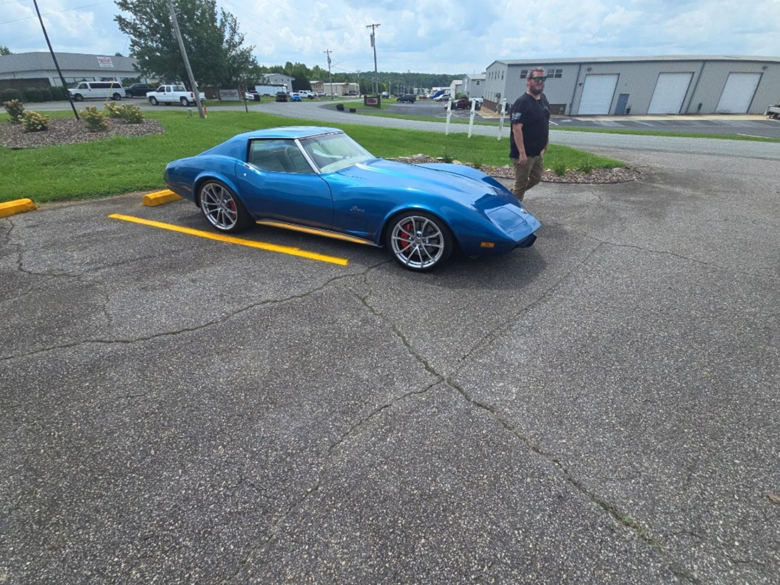 A man is standing next to a blue car in a parking lot.