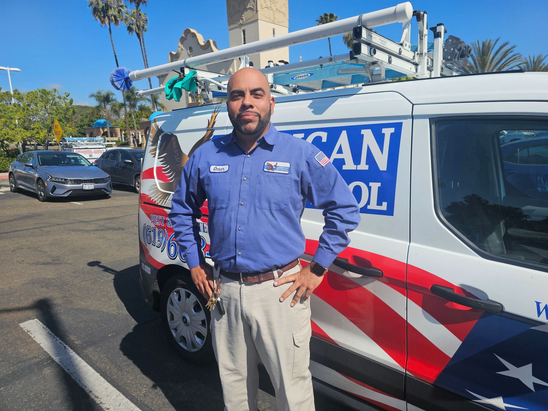 Man in blue work shirt stands by a van with American flag graphic. He has his hands on his hips.