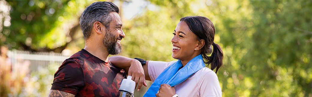 Two people smiling and talking outdoors, holding hands in a sunlit garden.