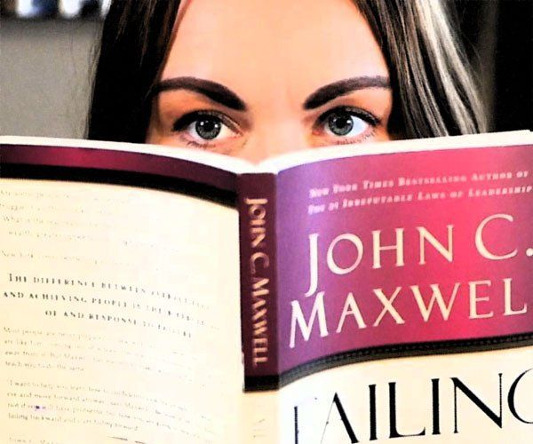 Woman peeks over a John C. Maxwell book, showing only her eyes and the cover text.