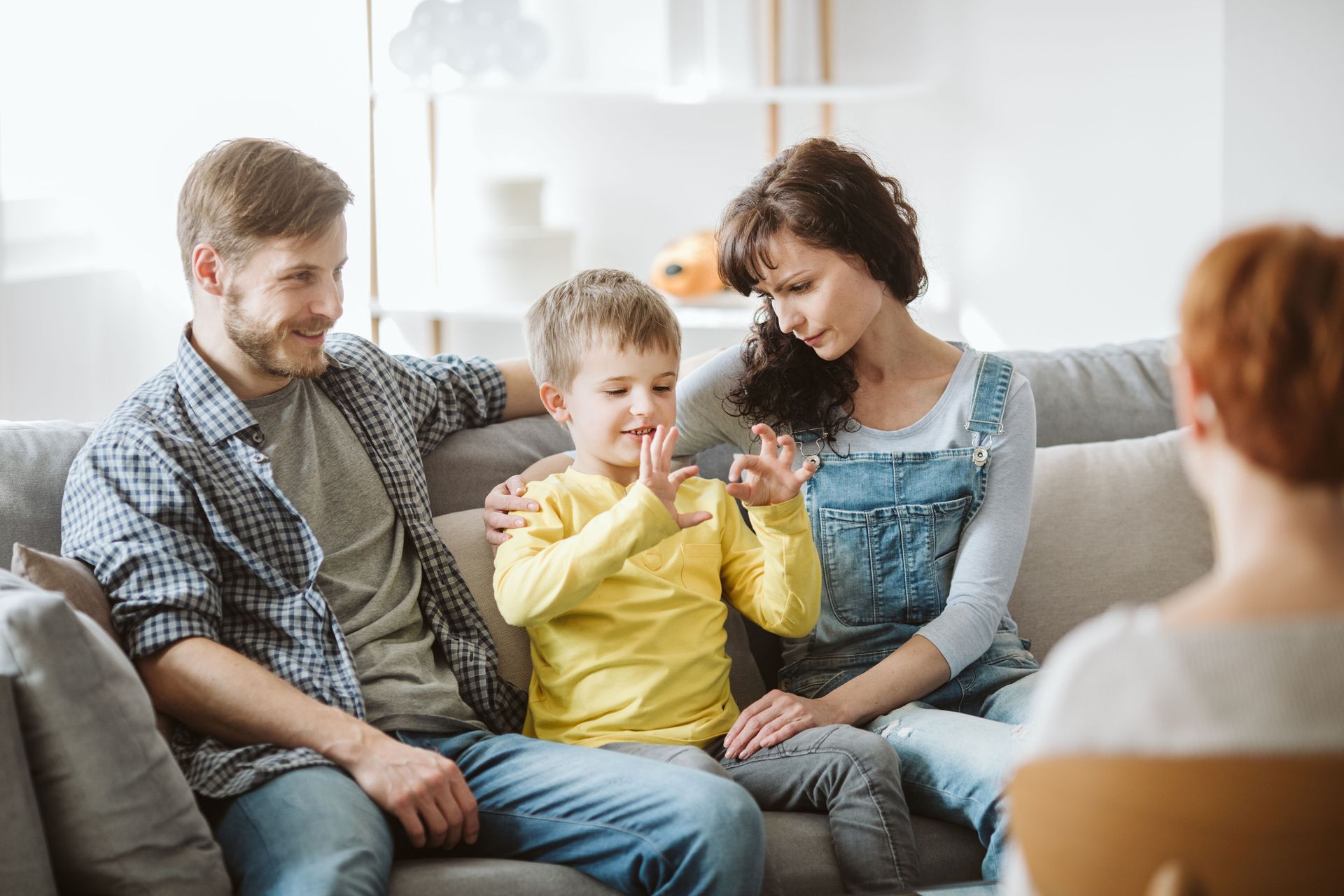 Family sitting on a couch, with a child in a yellow shirt holding a small object while adults watch nearby