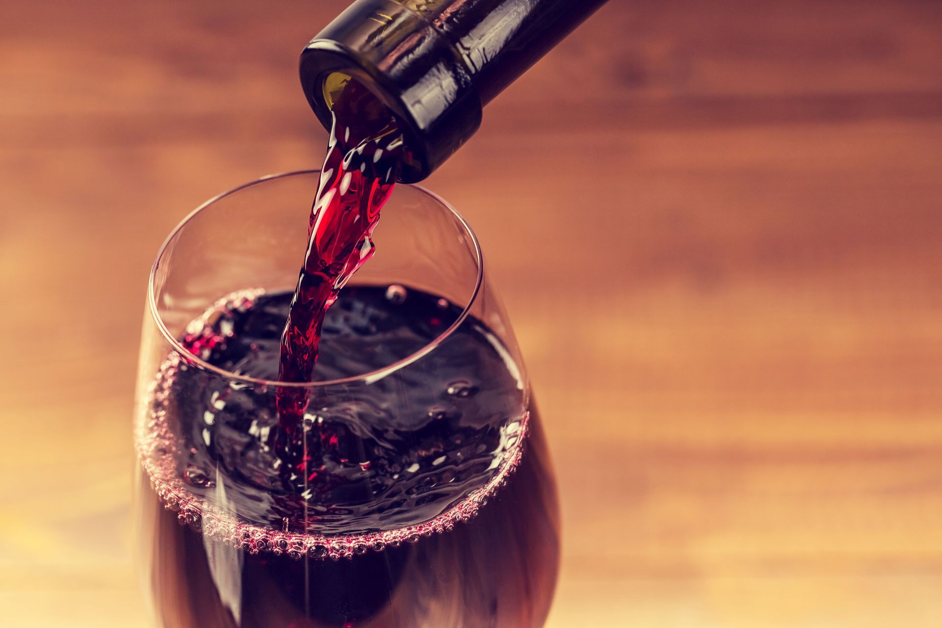 Red wine being poured into a glass on a wooden table, with a warm blurred background