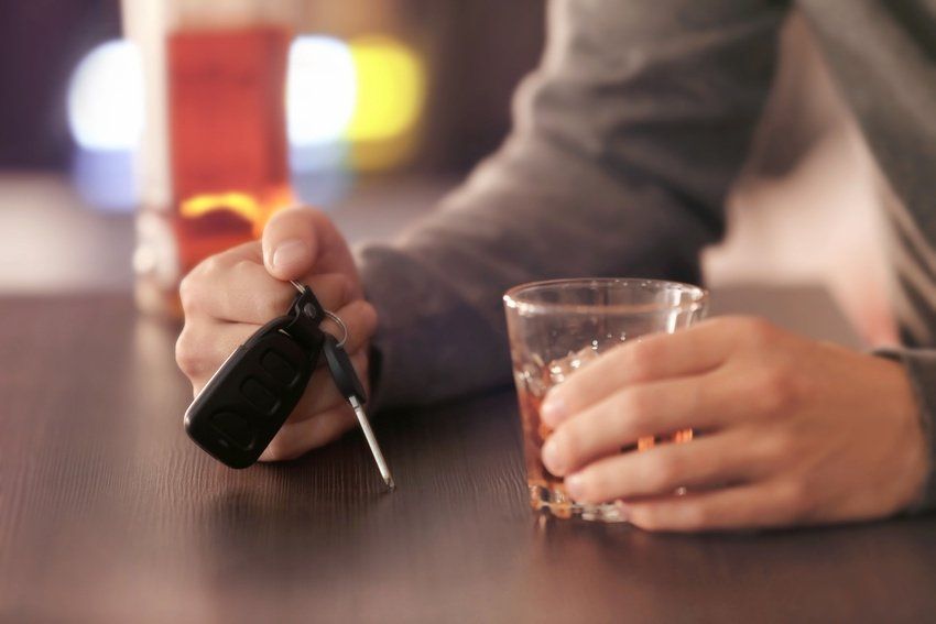 Hand holding a car key beside a glass on a table in a dimly lit bar or restaurant