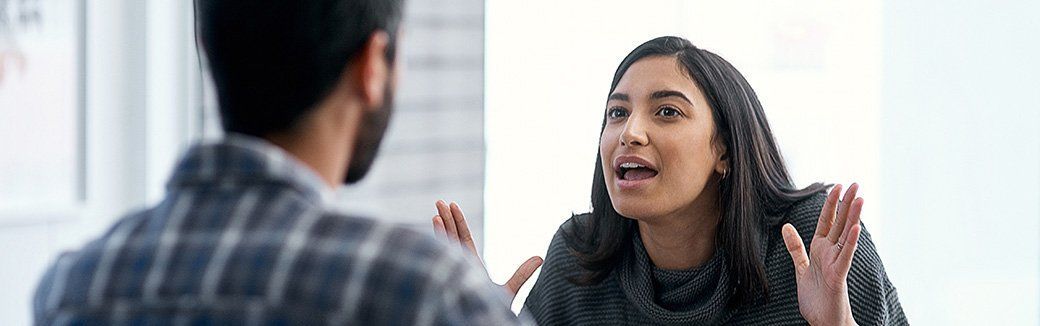 Two people in a bright office, one speaking animatedly across a table