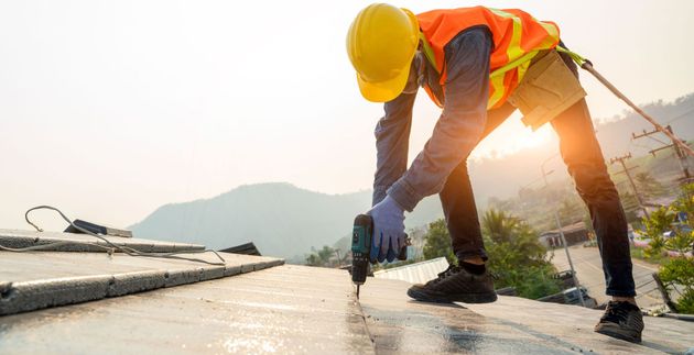 Construction worker in a yellow hard hat and orange vest measuring concrete on a rooftop at sunrise